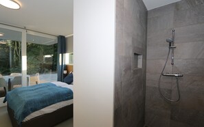 A modern bedroom with a large bed, a glass door leading to an outdoor area, and a shower with a handheld showerhead. - Horizon 99 comfortable villa for a majestic vacation (Renesse)