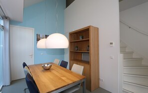 Un coin repas comprenant une table en bois, des chaises, un luminaire suspendu, une bibliothèque en bois et un escalier.