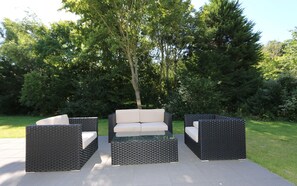 Un espace extérieur aménagé avec un canapé et deux fauteuils, entouré de verdure.
