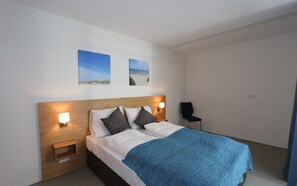 Une chambre d’hôtel avec un lit, deux lampes fixées au mur, une table de chevet et deux tableaux encadrés accrochés au mur.