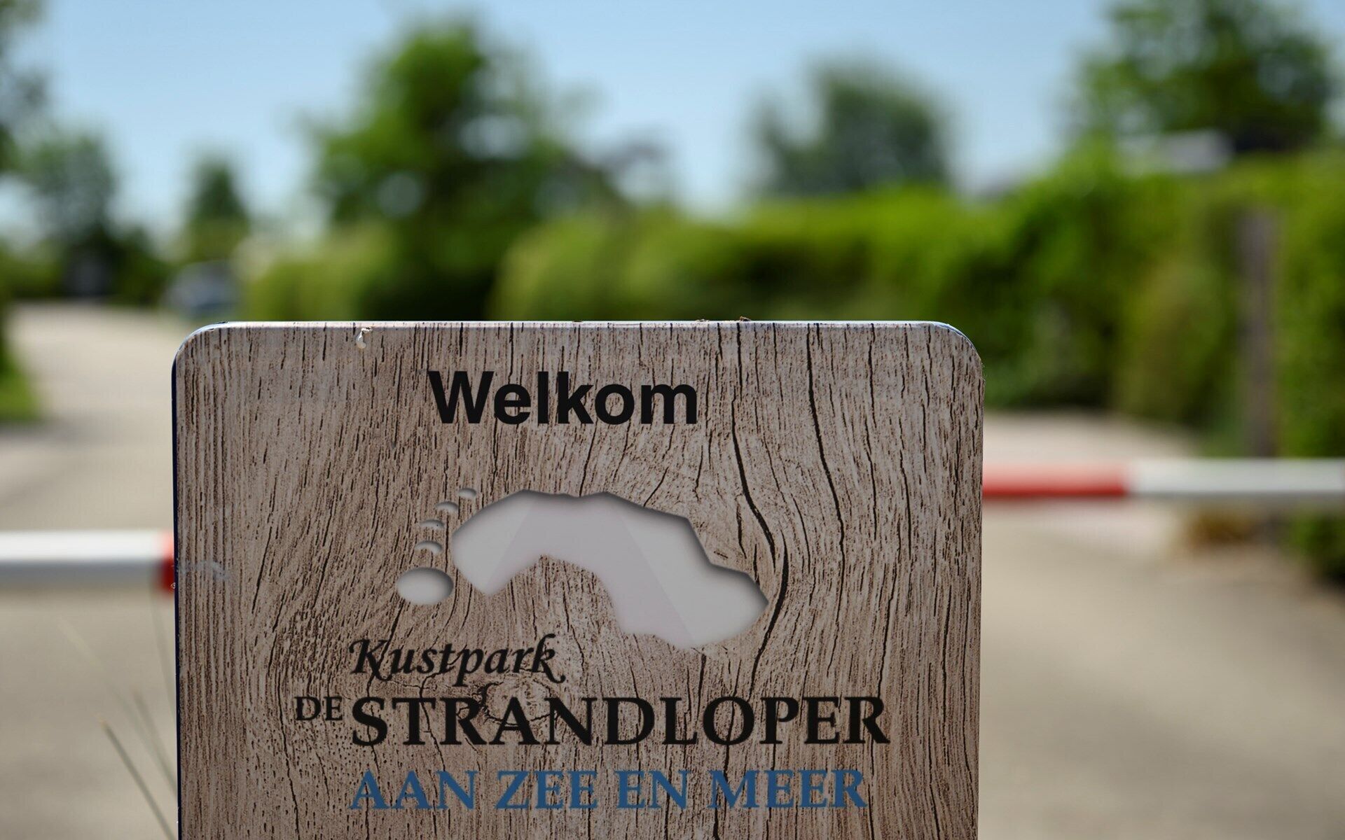 Une pancarte d’accueil en bois, ornée d’une découpe représentant un cheval, indiquant l’emplacement d’un parc équestre appelé « Kustpark de Strandlooper ».