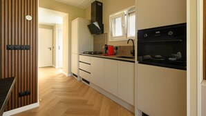 Ett modernt kök med ett fiskbensmönstrat golv, en inbyggd ugn och en röd kaffemaskin.