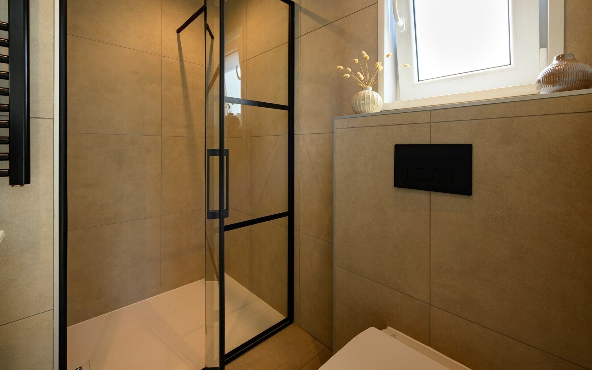 A bathroom with a glass shower enclosure, a towel rack, a small shelf with decorative items, and a wall-mounted control panel.