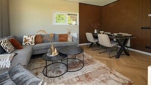 Ett modernt vardagsrum med en grå soffa, ett soffbord och en matplats med en väggpanel i trä.