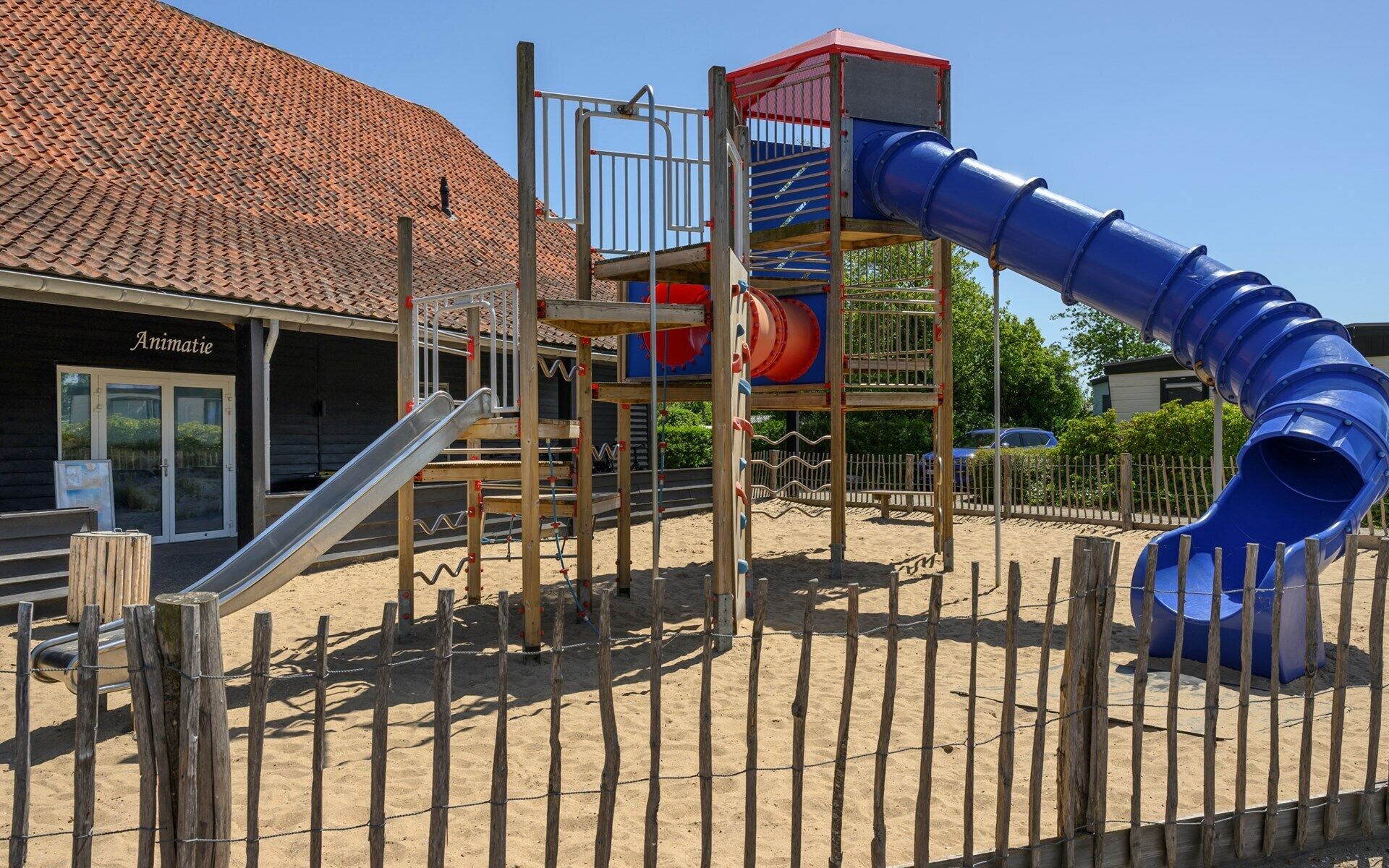 Een speeltuin met een glijbaan, klimconstructies en een gebouw met de tekst 'Animatie' op de achtergrond.