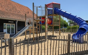 Un parque infantil con tobogán, estructuras de escalada y un edificio con la leyenda 'Animatie' al fondo.