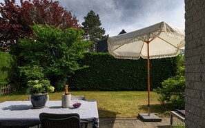 A patio with a table, chairs, a bottle of champagne, a bowl of strawberries, and a decorative umbrella. - Zeeduin "Neeltje" detached holiday home with large private garden (Burgh-Haamstede)