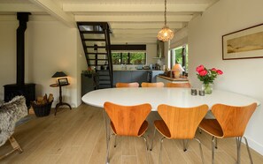 A modern kitchen with a central island, a dining area with wooden chairs, a staircase, and a large window. - Zeeduin "Neeltje" detached holiday home with large private garden (Burgh-Haamstede)