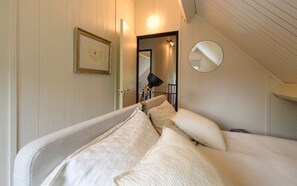 Ein Schlafzimmer mit einem Bett, Kissen, einer Nachttischlampe, einem gerahmten Bild, einem Spiegel und einer Tür zu einem anderen Raum.