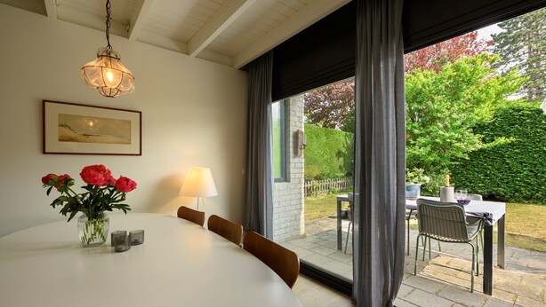 Un comedor con una mesa, sillas, un jarrón con flores, una lámpara y vistas al exterior.