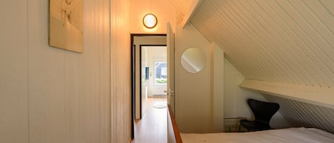 A bedroom with a sloped ceiling, a bed, a chair, and a door leading to a hallway.