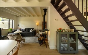 A living room with a sofa, a dining table, a fireplace, and a staircase. - Zeeduin "Neeltje" detached holiday home with large private garden (Burgh-Haamstede)
