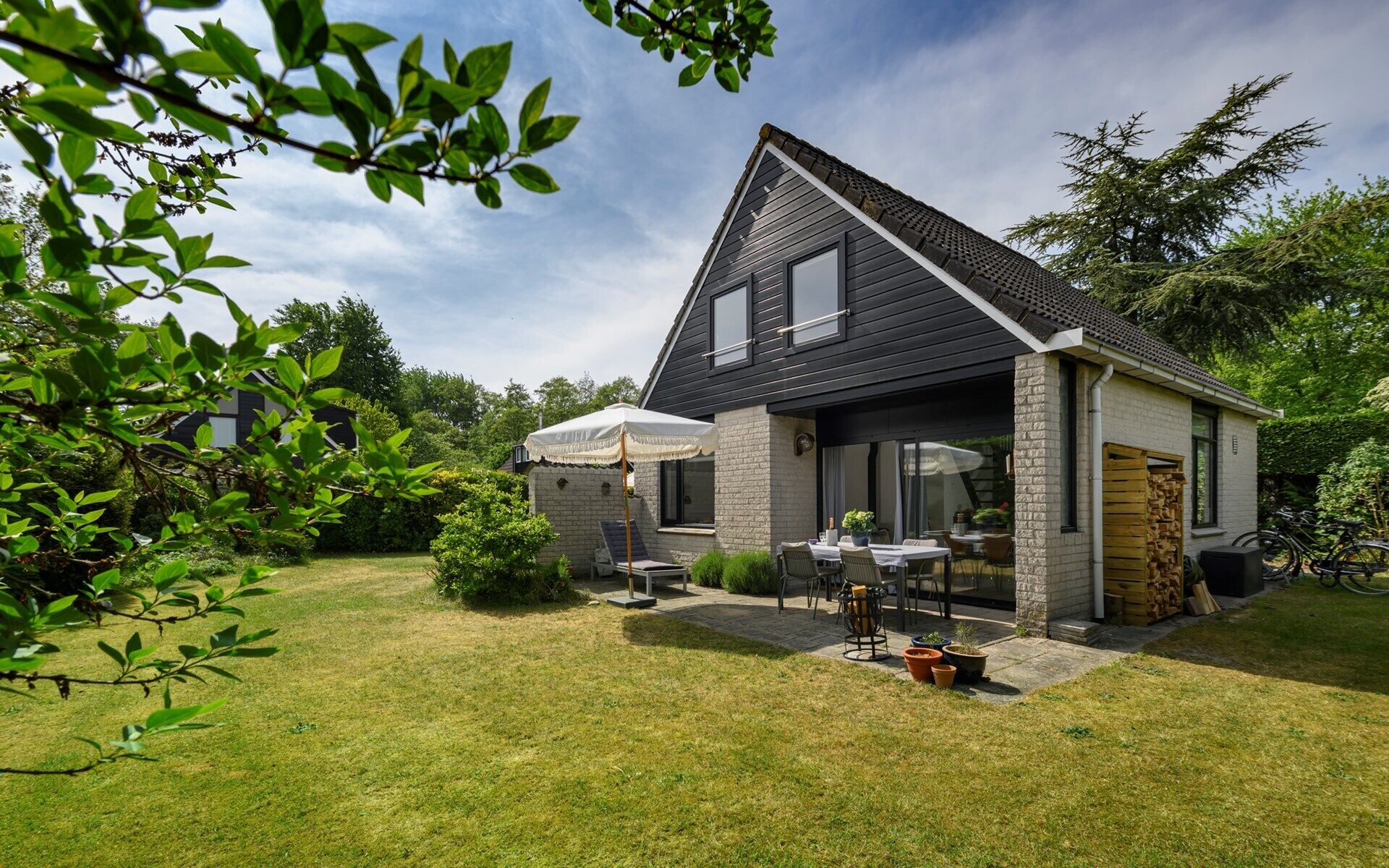 Une maison moderne à deux étages, dotée d’un toit en pente, d’une terrasse avec mobilier d’extérieur et d’une pelouse bien entretenue.