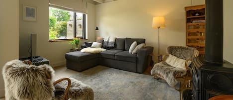 Ett mysigt vardagsrum med en soffa, en mjuk fåtölj, en öppen spis och en bokhylla.
