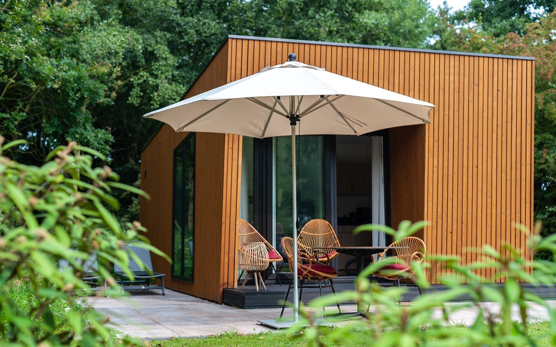 A modern wooden building with a large umbrella, wicker chairs, and a patio area.
