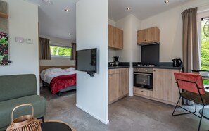 A compact room with a bed, a TV, a kitchenette, and a dining area. - Hoeve Lodge "De Meidoorn" (Burgh-Haamstede)