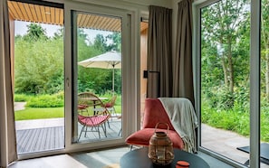 A room with a large sliding glass door leading to an outdoor patio with a table, chairs, and a garden view. - Hoeve Lodge "De Meidoorn" (Burgh-Haamstede)