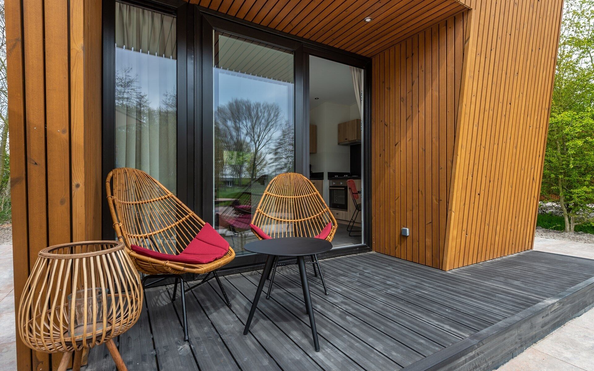 A modern outdoor seating area with wicker chairs and a table, a wooden deck, and a glass door leading to a kitchen.