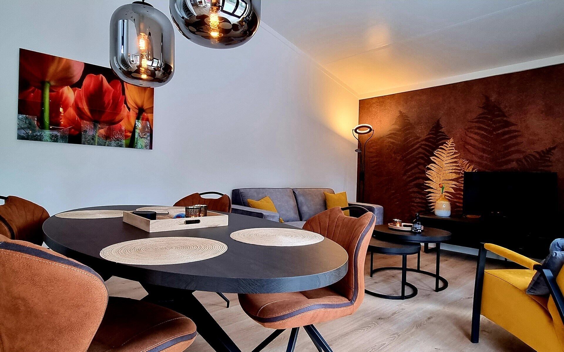 Een moderne woonkamer met een ronde eettafel, comfortabele zithoek, een flatscreen televisie en een groot wanddecor.
