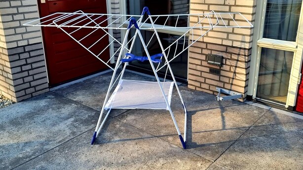 A metal laundry basket with blue handles on a concrete surface.