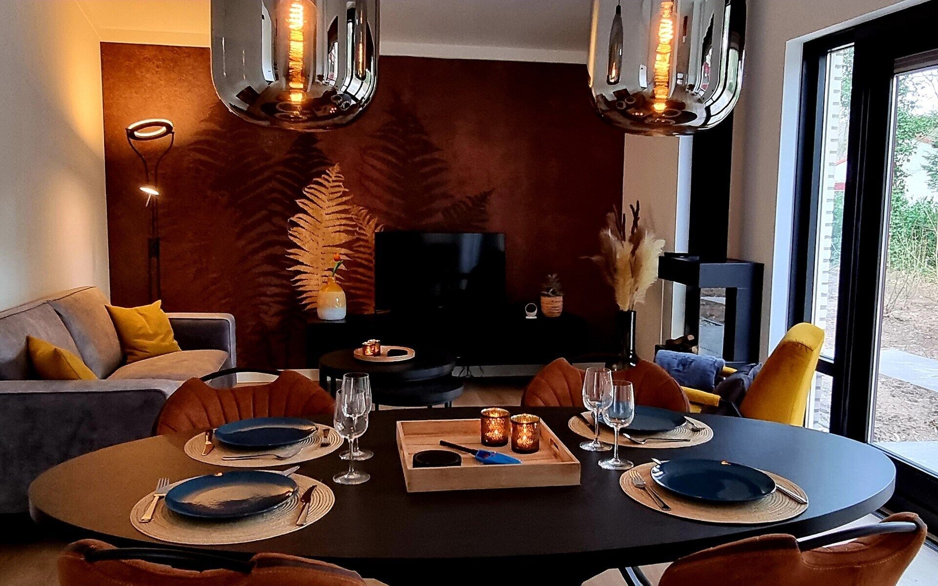 A dining area with a round table set for four, a television in the background, and a large window offering a view.
