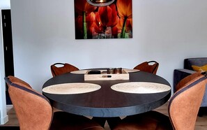 Une table de salle à manger ronde, avec quatre chaises, un chandelier central et une œuvre d’art encadrée au-dessus.