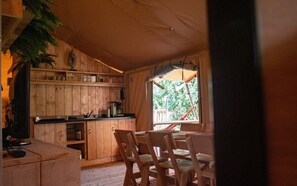 Ein Holzblockhaus-Innenraum mit Küchenbereich, Esstisch, Stühlen und einem Fenster mit Blick auf Grünflächen.