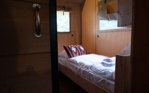 Ein Einzelbett mit einem gemusterten Kopfkissen, einem Holzkopfstück und einem Fenster mit Vorhängen.