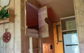 A room with a wooden ceiling, a white refrigerator, and a door with a towel hanging on it.