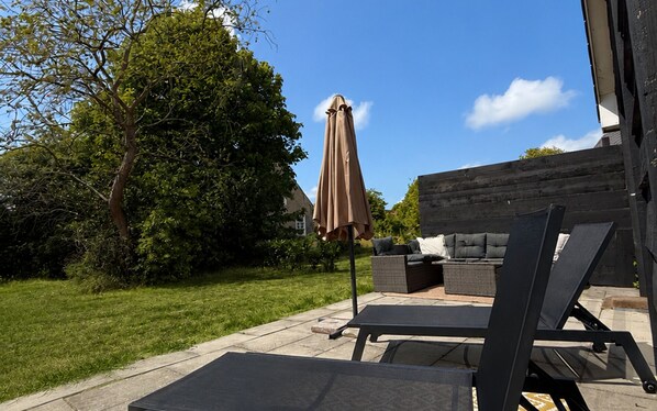 Un patio al aire libre con zona de estar, una mesa y un gran paraguas.