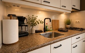 A modern kitchen with a granite countertop, stainless steel sink, and a coffee maker.