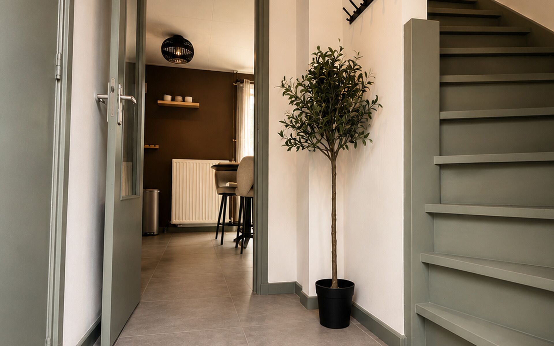 A hallway with a potted tree, a radiator, and a staircase.
