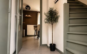A hallway with a potted tree, a radiator, and a staircase.