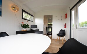 A modern dining area with a white table, black chairs, a potted plant, and a television on a stand.