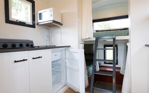 Cocina compacta con estufa, microondas y refrigerador. Una escalera lleva a una zona de dormir en loft.