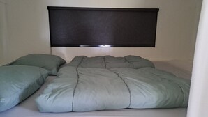 A bed with a grey duvet and pillows, a dark headboard, and a white wall.