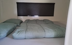 A bed with a grey duvet and pillows, a dark headboard, and a white wall.
