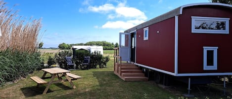 A red mobile home with a wooden deck and a picnic table.