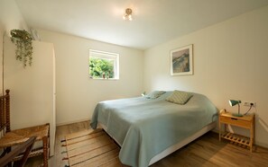 A bedroom with a bed, a window, a chair, a bedside table, and a lamp.