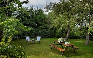 An outdoor setting with a picnic table and two chairs, surrounded by lush greenery.