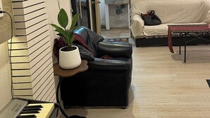 A living room with a piano, a black leather sofa, a white couch, a small table, and a potted plant. - Rural Stay Baan Mea Pen  Nature Retreat  (Chiang Rai)