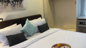 Un lit bien fait, recouvert d’une courtepointe blanche, avec des oreillers et un panier de fruits.