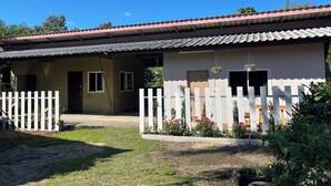 A two-story building with a red-tiled roof, a white picket fence, and a garden area with potted plants and flowers. - Rural Stay Baan Mea Pen  Nature Retreat  (Chiang Rai)