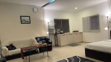 A compact living space with a sofa, a dining table, a kitchenette, and a bed.