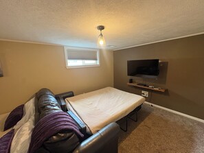A room with a sofa, a foldable bed, a television, and a ceiling light.