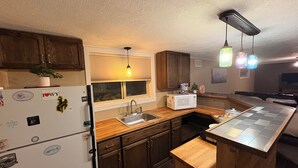 A compact kitchen with wooden cabinets, a built-in microwave, a sink, and a window with blinds.