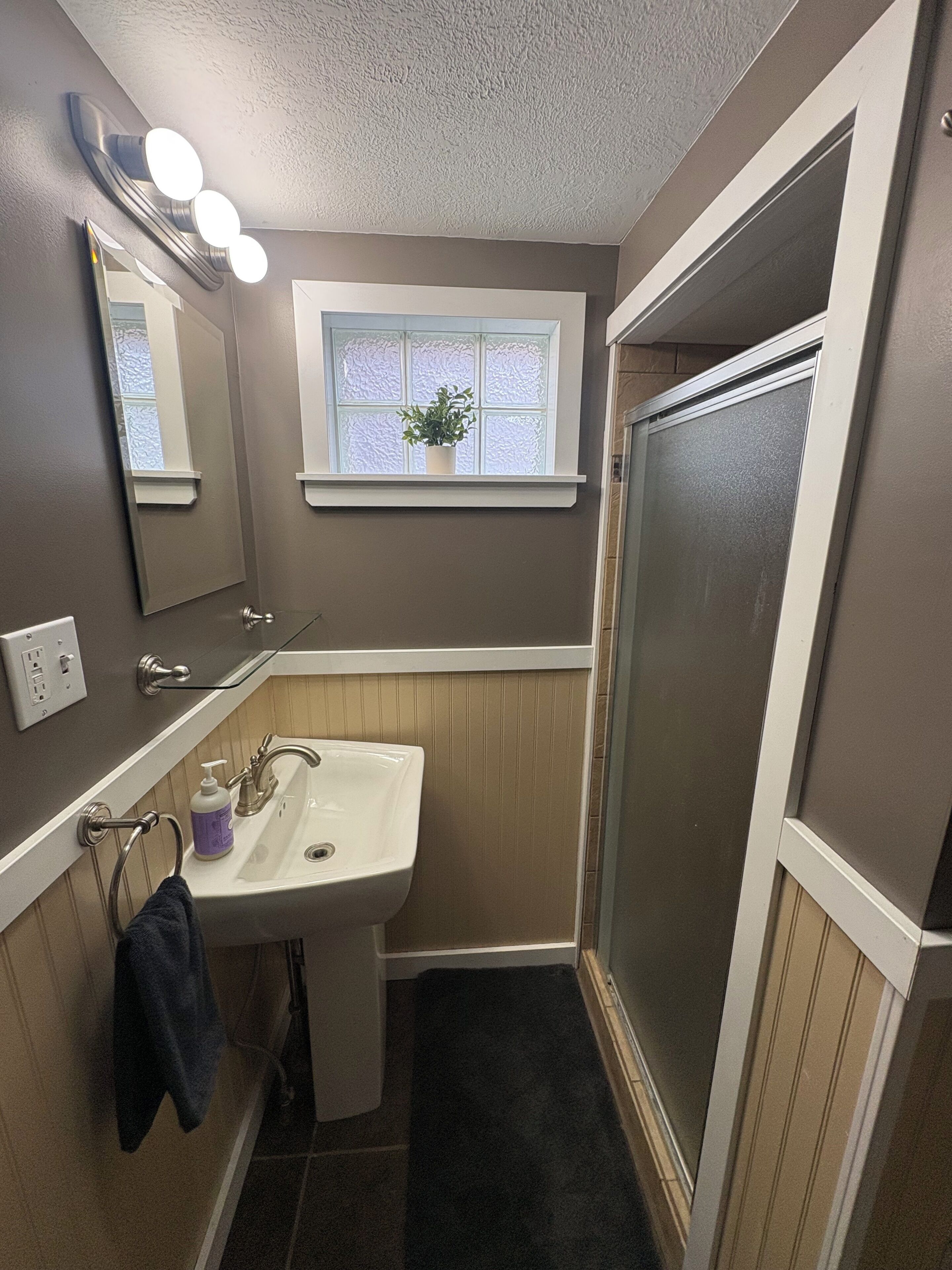 Une salle de bain avec un lavabo, un miroir, une fenêtre et une douche.