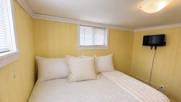 A bedroom with a bed, a window, and a wall-mounted TV.
