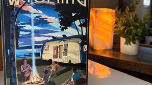 A framed picture of a camping scene with a camper and people around a fire, titled 'WYOMING,' on a white surface.