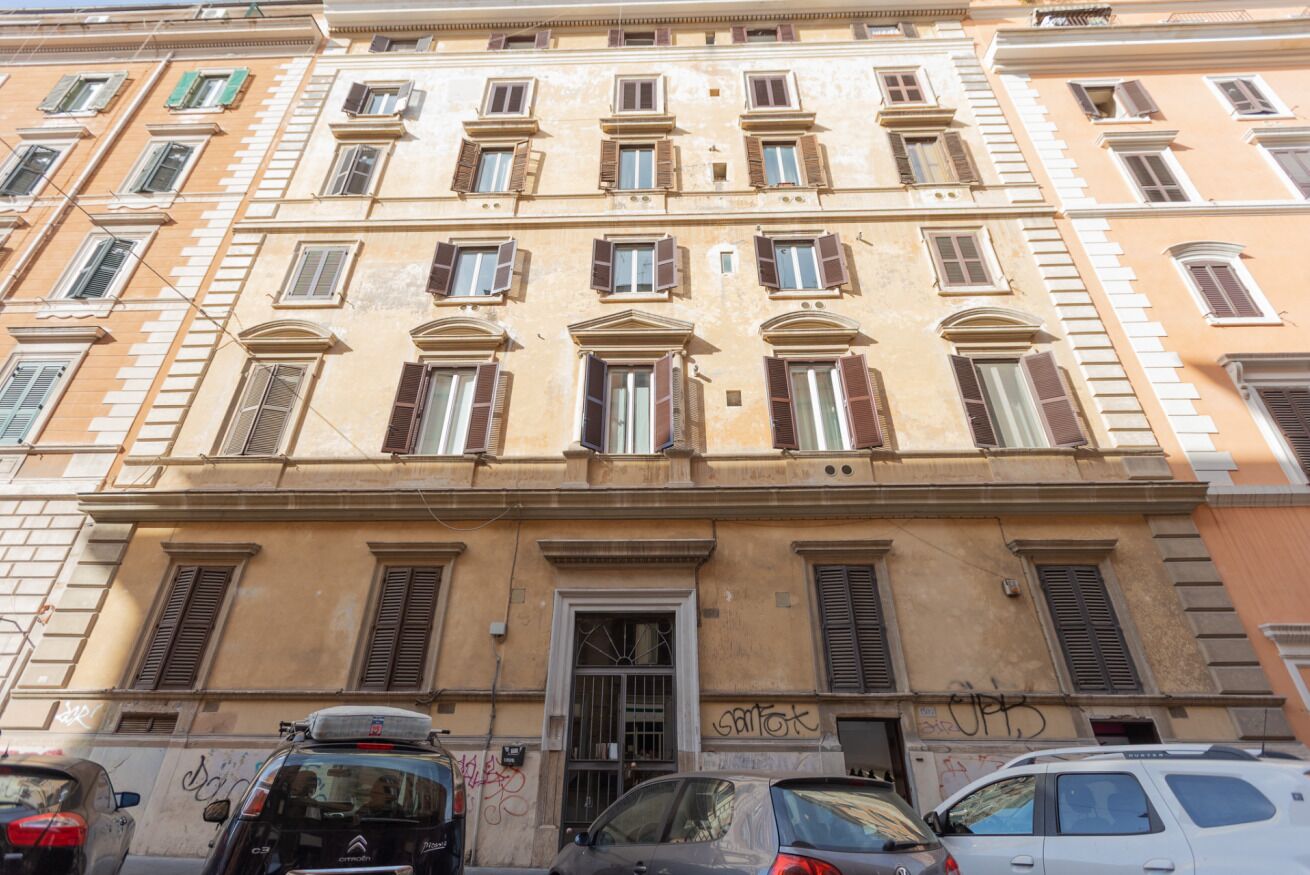 A multi-story building with a central entrance, multiple windows with shutters, and a visible door.